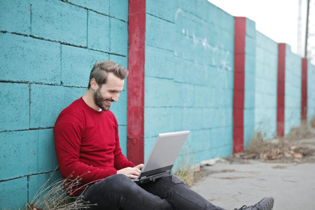 Man Leaning Against Wall Using Laptop-Mailer Online