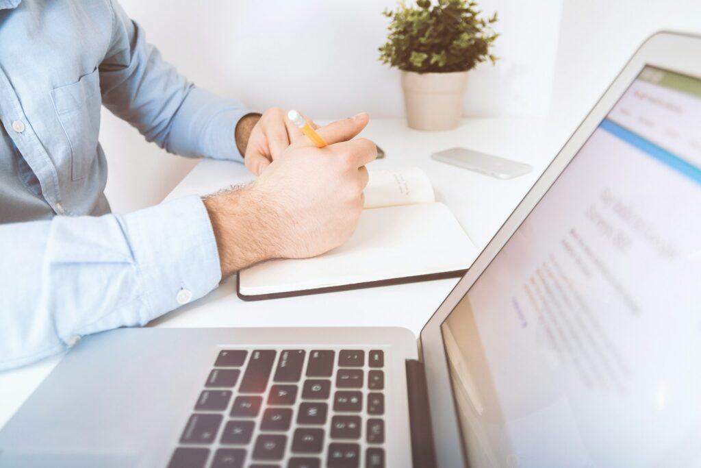 person writing on white notebook-Email Marketing Reviews