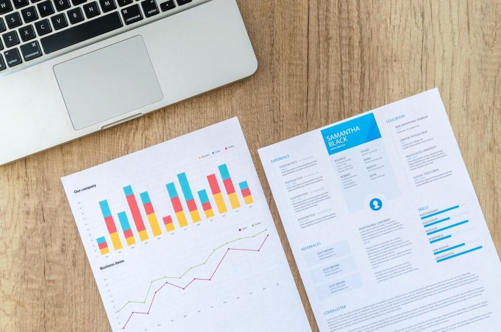 Top view of a laptop, charts, and resume on a wooden desk, showcasing business analysis and job application. low-budget marketing campaigns