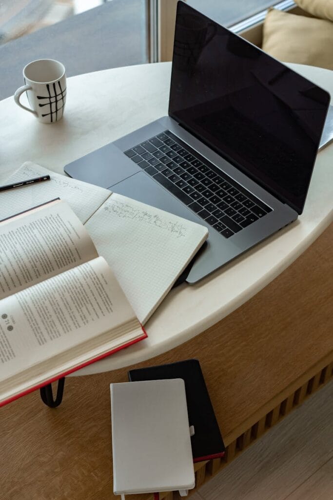 A cozy indoor workspace featuring a laptop, open book, notepad, and coffee, perfect for studying or remote work.Free business email without domain